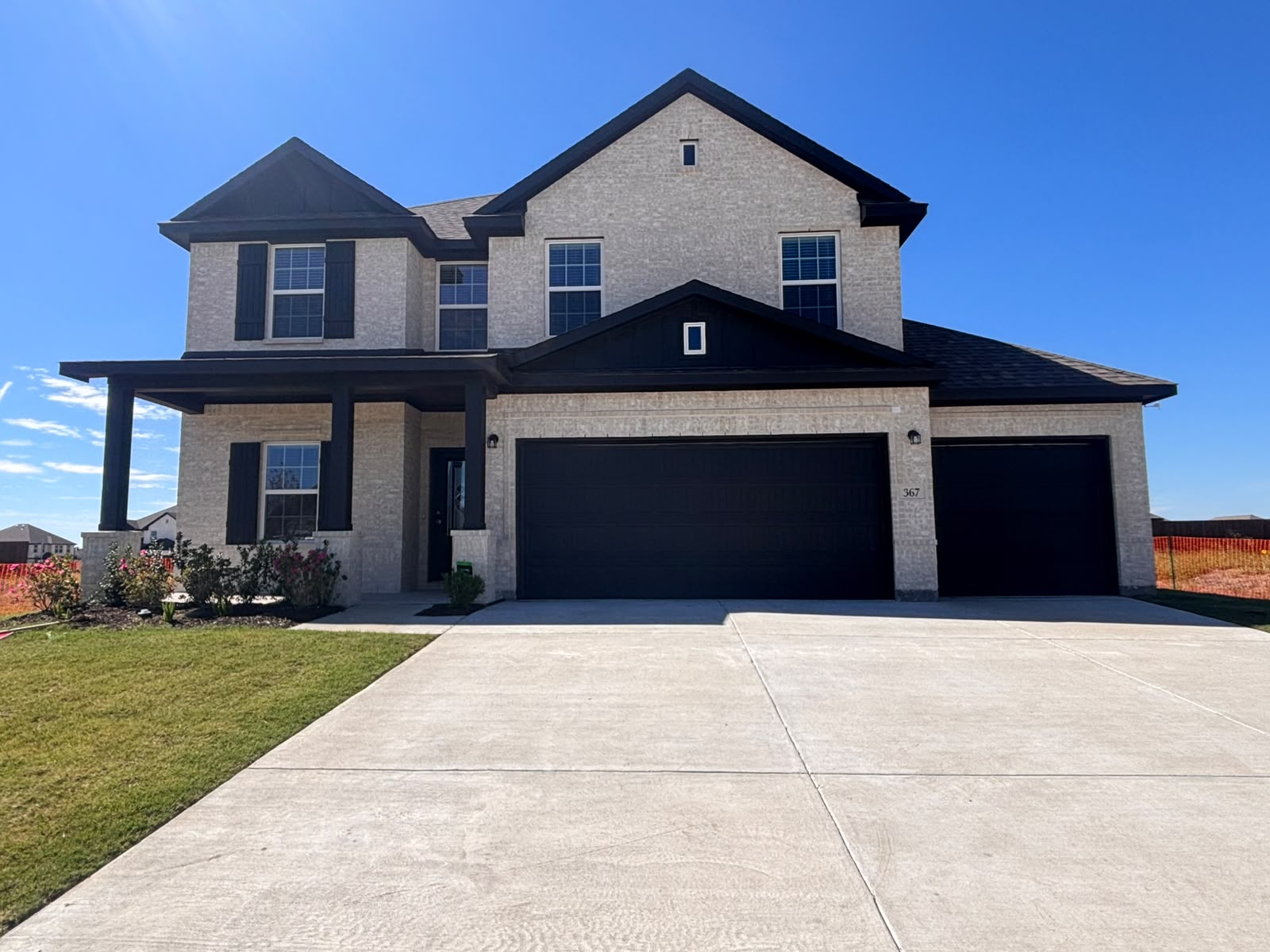 New two-story home in light brick with black trim and a wide driveway